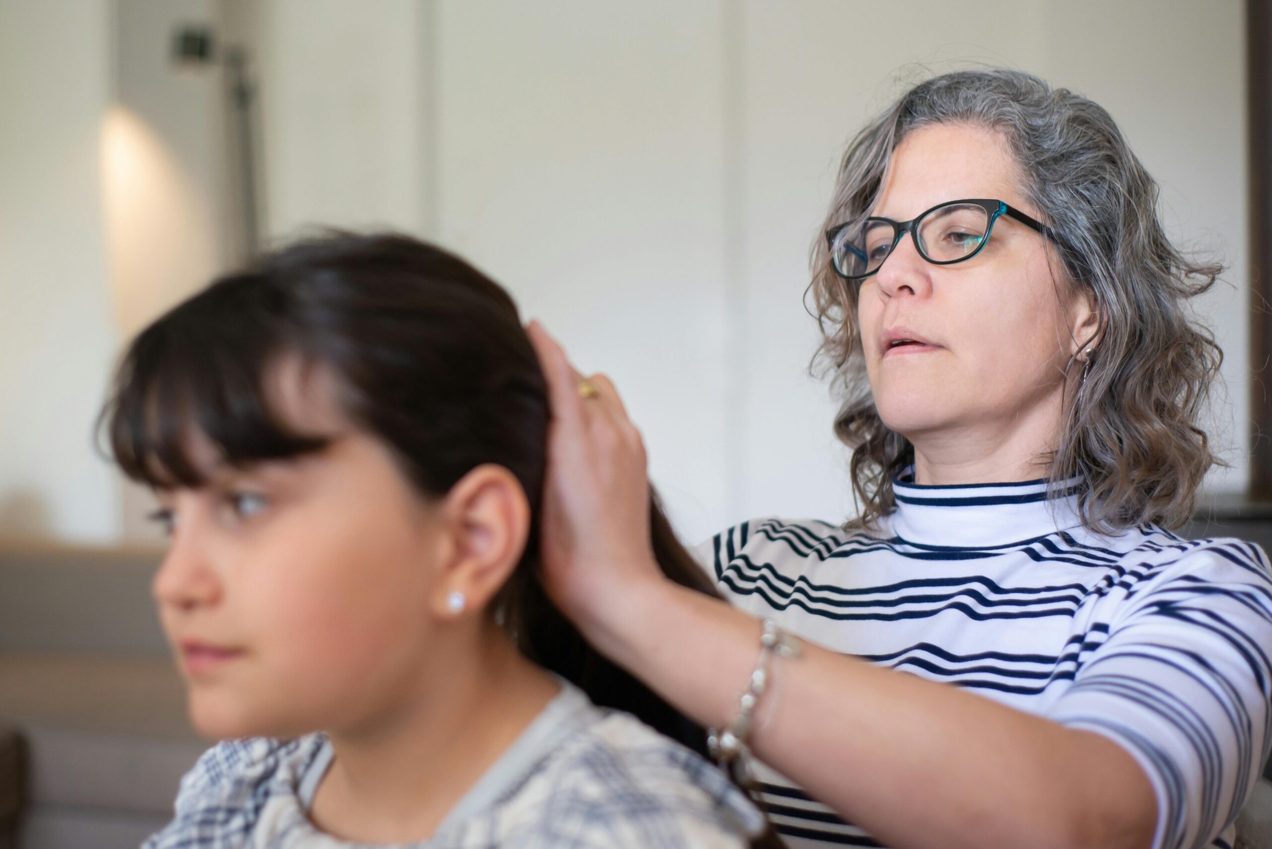 A mother attentively fixing her daughter's hair indoors, showcasing a loving bond.
